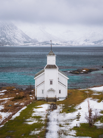 Aerial view of the white Gimsøy Church standing out against the aqua sea and snow dusted landscape Gimsøysand Nordland Norway. Aerial view of the white Gimsøy Church standing out against the aqua sea and snow dusted landscape Gimsøysand Nordland Norway.