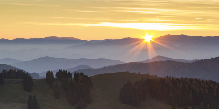View of golden sunlight piercing through the hazy blue mountains casting long shadows across the green hillsides Sommeralm Steiermark Austria. View of golden sunlight piercing through the hazy blue mountains casting long shadows across the green hillsides Sommeralm Steiermark Austria.