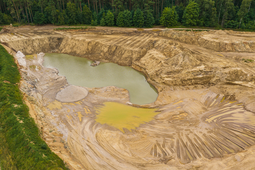 Aerial view of a gravel pit with a small pond sandy terrain and tire tracks surrounded by a forest in Tczew Pomeranian Voivodeship Poland. Aerial view of a gravel pit with a small pond sandy terrain and tire tracks surrounded by a forest in Tczew Pomeranian Voivodeship Poland.
