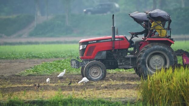 View of a red tractor plowing a field with workers Bangladesh.