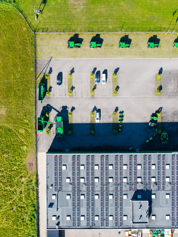 Aerial view of a farm equipment supplier featuring a row of green tractors parked cars and a building with solar panels on the roof in Kekava Kekava Municipality Latvia. Aerial view of a farm equipment supplier featuring a row of green tractors parked cars and a building with solar panels on the roof in Kekava Kekava Municipality Latvia.