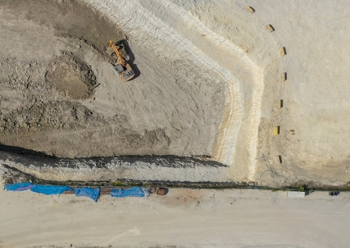 Aerial view of a yellow excavator digging in a large construction site with trenches and blue tarps in Avcilar Istanbul Turkiye. Aerial view of a yellow excavator digging in a large construction site with trenches and blue tarps in Avcilar Istanbul Turkiye.