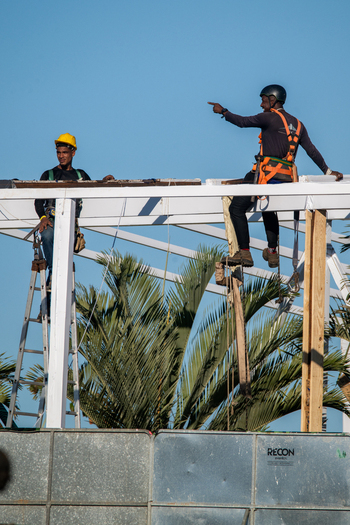 Rio de Janeiro Brazil 20 June 2026 View of two construction workers in safety harnesses and helmets working on a white metal frame structure with palm trees in the background. Rio de Janeiro Brazil 20 June 2026 View of two construction workers in safety harnesses and helmets working on a white metal frame structure with palm trees in the background.