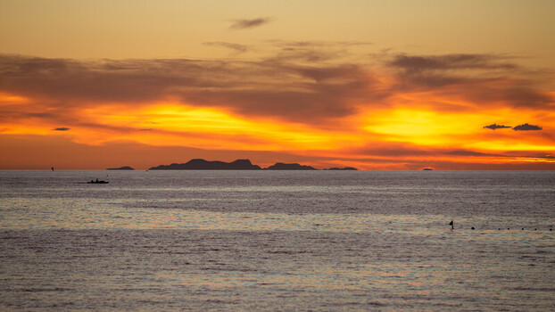 View of Bantayan Island at sunset with a small boat silhouetted on the calm ocean waters under a vibrant orange and yellow sky in Cebu Central Visayas Philippines. View of Bantayan Island at sunset with a small boat silhouetted on the calm ocean waters under a vibrant orange and yellow sky in Cebu Central Visayas Philippines.