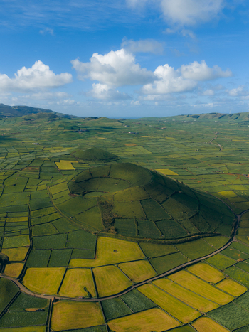 Aerial view of Pico Dona Joana geodesico volcanic crater surrounded by a patchwork of green agricultural fields under a blue sky with white clouds Feteira Acores Portugal.