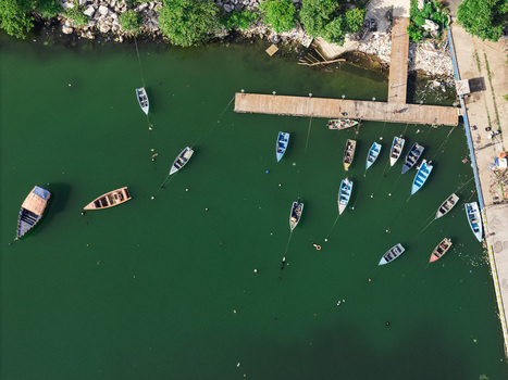 Aerial view of small fishing boats moored in the green waters of a harbor near a wooden pier in Bajos de Haina San Cristobal Province Dominican Republic.