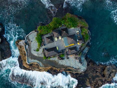 Aerial view of Tanah Lot Temple with traditional Balinese architecture and dark tiled roofs on a rocky outcrop surrounded by crashing ocean waves in Kecamatan Kediri Bali Indonesia. Aerial view of Tanah Lot Temple with traditional Balinese architecture and dark tiled roofs on a rocky outcrop surrounded by crashing ocean waves in Kecamatan Kediri Bali Indonesia.