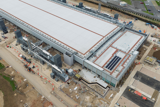 Aerial view of a large data center facility featuring extensive rooftop HVAC systems solar panels and surrounding construction site infrastructure in the United Kingdom.