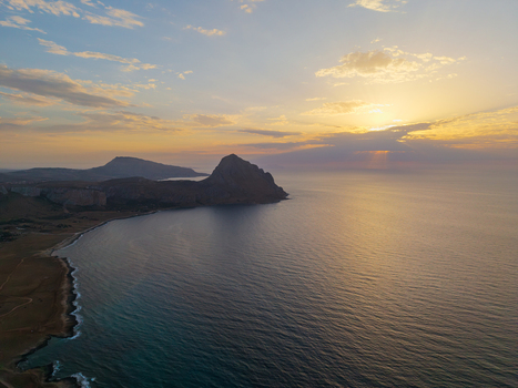 Aerial view of Mount Cofano rising above the calm Mediterranean Sea during a golden sunset with soft clouds and coastal cliffs in Palermo Sicily Italy. Aerial view of Mount Cofano rising above the calm Mediterranean Sea during a golden sunset with soft clouds and coastal cliffs in Palermo Sicily Italy.