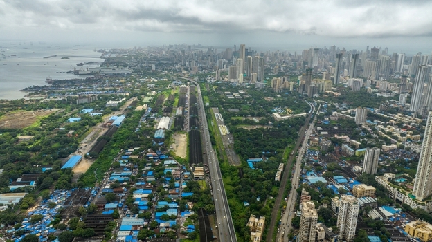 Aerial view of the sprawling urban landscape of Mumbai featuring high rise buildings dense residential areas and a highway stretching towards the coastline in Mumbai Maharashtra India.