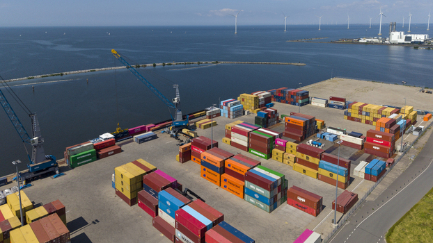 Aerial view of TMA Terminals Lelystad featuring colorful shipping containers large cranes and wind turbines in the background near the water in Lelystad Flevoland Netherlands. Aerial view of TMA Terminals Lelystad featuring colorful shipping containers large cranes and wind turbines in the background near the water in Lelystad Flevoland Netherlands.