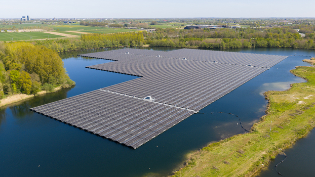 Aerial view of a large floating solar farm on a calm lake surrounded by lush green trees and rural landscape under a clear sky in Zwolle Overijssel Netherlands. Aerial view of a large floating solar farm on a calm lake surrounded by lush green trees and rural landscape under a clear sky in Zwolle Overijssel Netherlands.