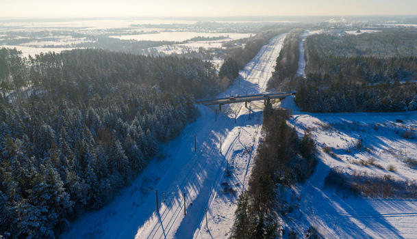 Aerial view of railway tracks cutting through a dense snow covered evergreen forest with a bridge overpass under bright winter sunlight Lithuania. Aerial view of railway tracks cutting through a dense snow covered evergreen forest with a bridge overpass under bright winter sunlight Lithuania.