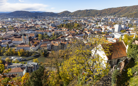 View of colorful buildings scattered between trees with yellow foliage and rolling hills meeting a clear blue sky in the distance Graz Styria Austria. View of colorful buildings scattered between trees with yellow foliage and rolling hills meeting a clear blue sky in the distance Graz Styria Austria.