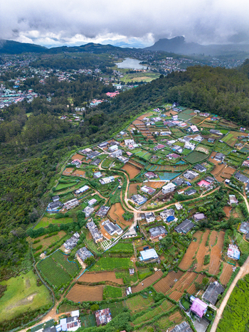 Aerial view of Nuwara Eliya featuring terraced tea plantations scattered houses and lush green hills under a cloudy sky in Nuwara Eliya Central Province Sri Lanka. Aerial view of Nuwara Eliya featuring terraced tea plantations scattered houses and lush green hills under a cloudy sky in Nuwara Eliya Central Province Sri Lanka.
