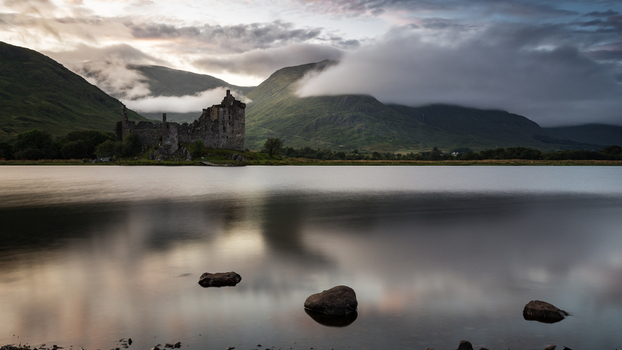 View of the historic Kilchurn Castle ruins on the shore of Loch Awe with misty mountains and low clouds Scotland.