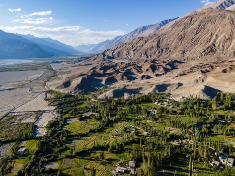 Aerial view of the lush green valley with agricultural fields and trees nestled among the arid rugged mountains of the Ladakh region in Ladakh Division Ladakh India. Aerial view of the lush green valley with agricultural fields and trees nestled among the arid rugged mountains of the Ladakh region in Ladakh Division Ladakh India.