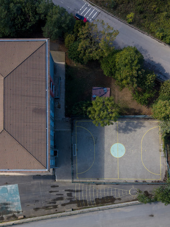 Aerial view of a modern building adjacent to a paved sports court with yellow markings surrounded by lush green trees and a nearby road in Istanbul Istanbul Turkiye. Aerial view of a modern building adjacent to a paved sports court with yellow markings surrounded by lush green trees and a nearby road in Istanbul Istanbul Turkiye.