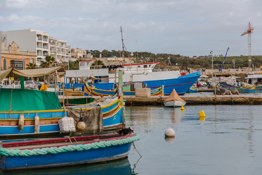 View of vibrant blue and yellow boats bobbing gently in the calm harbor waters against a backdrop of quaint buildings Marsaxlokk Malta. View of vibrant blue and yellow boats bobbing gently in the calm harbor waters against a backdrop of quaint buildings Marsaxlokk Malta.