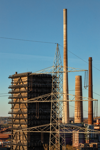 View of industrial chimneys and a high voltage power pylon standing against a clear blue sky at an old steel mill site in Duisburg North Rhine Westphalia Germany.