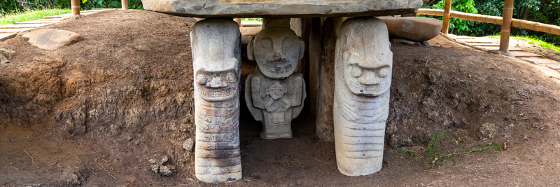View of ancient stone statues at San Agustin Archaeological Park featuring intricate monolithic carvings set into the earth ground under a bamboo shelter in San Agustin Huila Colombia. View of ancient stone statues at San Agustin Archaeological Park featuring intricate monolithic carvings set into the earth ground under a bamboo shelter in San Agustin Huila Colombia.