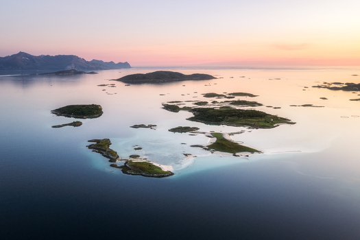 Aerial view of the islands of Sommaroy surrounded by clear blue water and sandy beaches with mountains in the distance under a soft sunset sky in Sommaroy Troms Norway. Aerial view of the islands of Sommaroy surrounded by clear blue water and sandy beaches with mountains in the distance under a soft sunset sky in Sommaroy Troms Norway.