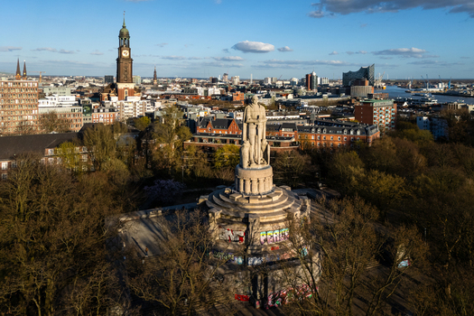 Aerial view of the Bismarck Monument with peace graffiti surrounded by lush trees with the St. Michael s Church and Elbphilharmonie in the background in Hamburg Hamburg Germany.