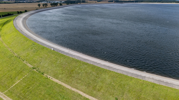Aerial view of Zarnowiec Pumped Storage Power Station reservoir with curved concrete embankment and grassy slopes in the rural landscape. Wejherowo County Pomeranian Voivodeship Poland.