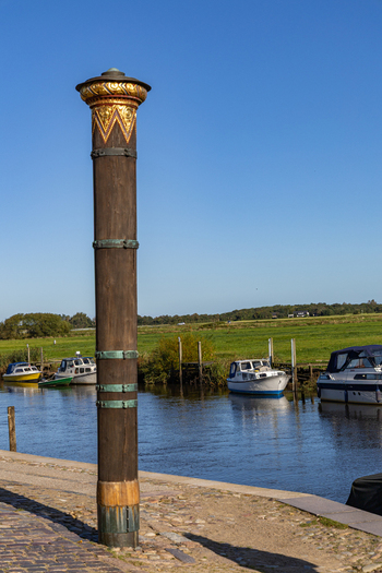 View of the Stormflodssojlen flood column on the waterfront with boats moored in the river under a clear blue sky in Ribe Denmark. View of the Stormflodssojlen flood column on the waterfront with boats moored in the river under a clear blue sky in Ribe Denmark.