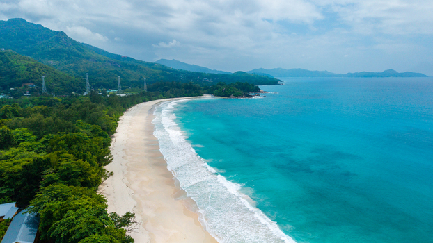 Aerial view of Grand Anse Mahe beach with turquoise waters white sand lush tropical vegetation and rolling hills in the background Grand Anse Mahe Seychelles. Aerial view of Grand Anse Mahe beach with turquoise waters white sand lush tropical vegetation and rolling hills in the background Grand Anse Mahe Seychelles.