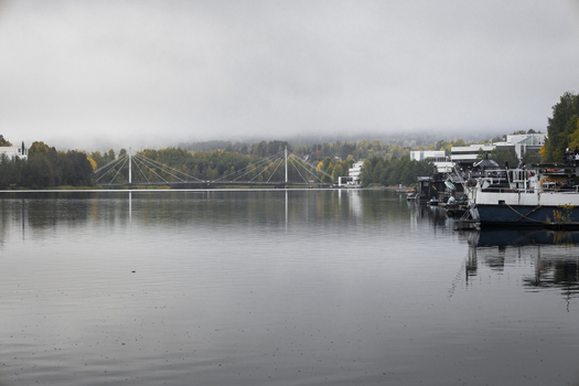 View of the Kuokkala Bridge spanning across the calm waters of Lake Jyvasjarvi with autumn trees and docked boats under a misty sky in Jyvaskyla Central Finland Finland.