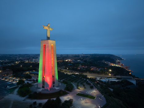 Aerial view of the Sanctuary of Christ the King illuminated in green and red lights at dusk overlooking the Tagus River in Almada Setubal Portugal. Aerial view of the Sanctuary of Christ the King illuminated in green and red lights at dusk overlooking the Tagus River in Almada Setubal Portugal.