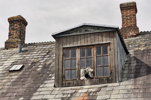 Viborg Denmark 07 August 2026 View of an old roof featuring a wooden dormer window weathered slate tiles and two brick chimneys against a cloudy sky. Viborg Denmark 07 August 2026 View of an old roof featuring a wooden dormer window weathered slate tiles and two brick chimneys against a cloudy sky.