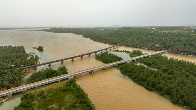 Aerial view of the Sharavati River bridges spanning the water with lush green vegetation and palm trees along the banks in Honnavar Karnataka India.