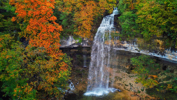 Aerial view of Herisson Waterfalls cascading down rugged cliffs surrounded by autumn foliage a symphony of orange and green Le Frasnois Bourgogne Franche Comt&eacute; France.