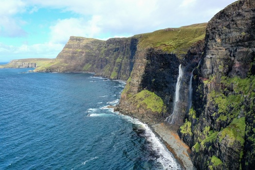 Aerial view of Mealt Falls cascading over the dramatic basalt cliffs of Kilt Rock into the sea on the Isle of Skye Scotland United Kingdom. Aerial view of Mealt Falls cascading over the dramatic basalt cliffs of Kilt Rock into the sea on the Isle of Skye Scotland United Kingdom.