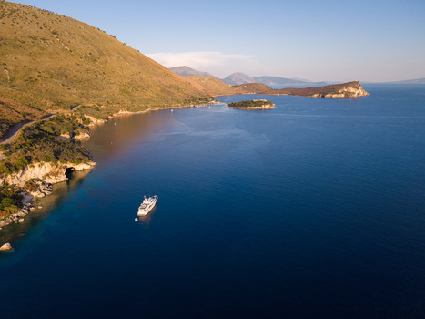 Aerial view of a white yacht anchored in the deep blue waters of Porto Palermo Bay surrounded by rugged green hills and a small island in Porto Palermo Qarku i Vlores Albania. Aerial view of a white yacht anchored in the deep blue waters of Porto Palermo Bay surrounded by rugged green hills and a small island in Porto Palermo Qarku i Vlores Albania.