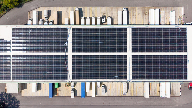 Aerial view of a logistics hub with solar panels on the warehouse roof and freight trucks parked at loading docks in Melegnano Lombardy Italy.