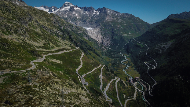 Aerial view of the winding switchbacks of the Grimsel Pass surrounded by steep alpine slopes and distant glaciers in Obergoms Valais Switzerland. Aerial view of the winding switchbacks of the Grimsel Pass surrounded by steep alpine slopes and distant glaciers in Obergoms Valais Switzerland.