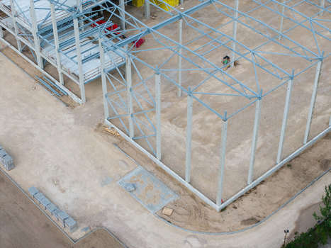 Aerial view of a construction site featuring a steel frame structure and concrete pillars rising from a gravel ground in Riga Latvia. Aerial view of a construction site featuring a steel frame structure and concrete pillars rising from a gravel ground in Riga Latvia.