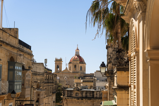 View of the Assumption of the Blessed Virgin Mary Parish Church dome and bell towers rising above traditional limestone buildings and balconies in Zebbug Gozo Region Malta. View of the Assumption of the Blessed Virgin Mary Parish Church dome and bell towers rising above traditional limestone buildings and balconies in Zebbug Gozo Region Malta.