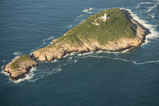 Aerial view of Ilha da Cotunduba featuring its iconic lighthouse rocky cliffs and lush green vegetation surrounded by the deep blue Atlantic Ocean in Rio de Janeiro Rio de Janeiro Brazil. Aerial view of Ilha da Cotunduba featuring its iconic lighthouse rocky cliffs and lush green vegetation surrounded by the deep blue Atlantic Ocean in Rio de Janeiro Rio de Janeiro Brazil.