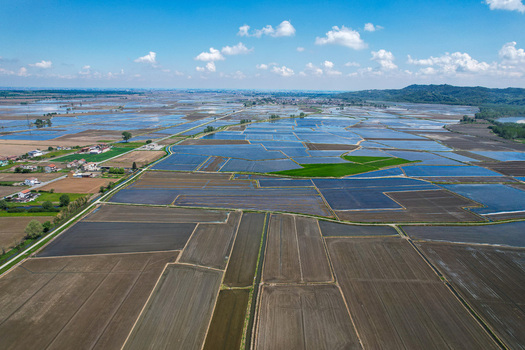 Aerial view of flooded rice fields reflecting the blue sky and clouds in the Vercelli plain near the historic Abbazia di Lucedio in Trino Piemonte Italy.