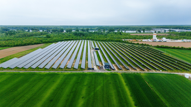 Aerial view of a large solar farm with rows of photovoltaic panels surrounded by lush green agricultural fields and dense forests near a river Sabac Vojvodina Serbia.