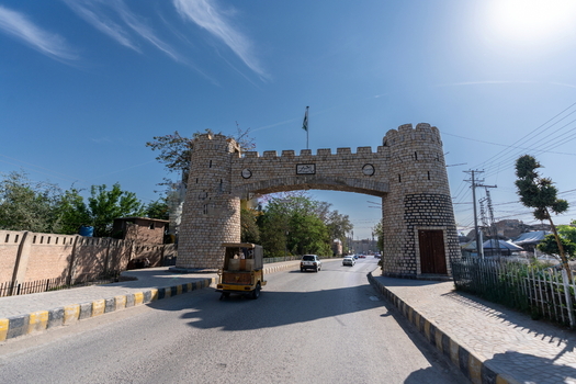 View of the historic Khyber Pass gate with a rickshaw and cars on the road under a clear blue sky in Khyber District Khyber Pakhtunkhwa Pakistan.