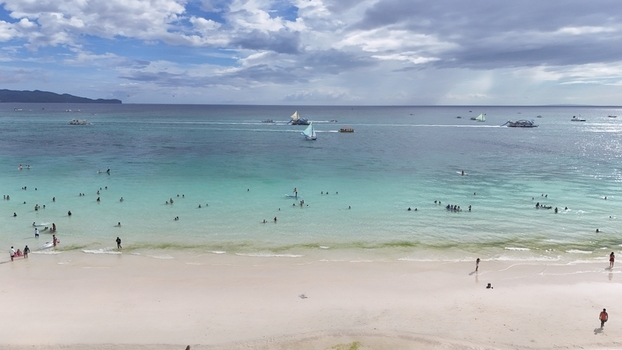 Malay Philippines 02 May 2026 Aerial view of Boracay Island featuring turquoise waters white sand beach with people swimming and traditional sailboats under a cloudy sky.