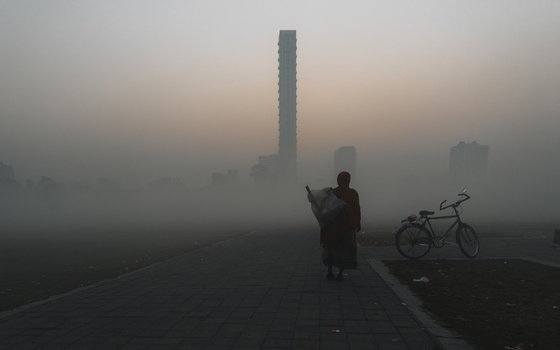 View of a solitary figure walks along a stone path shrouded in a dense fog with a bicycle nearby and a towering skyscraper in the distance Kolkata West Bengal India. View of a solitary figure walks along a stone path shrouded in a dense fog with a bicycle nearby and a towering skyscraper in the distance Kolkata West Bengal India.