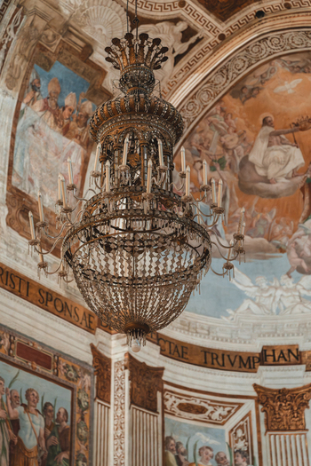 View of an ornate chandelier hangs beneath a frescoed ceiling depicting biblical scenes creating a striking contrast of light and shadow Taormina Sicily Italy. View of an ornate chandelier hangs beneath a frescoed ceiling depicting biblical scenes creating a striking contrast of light and shadow Taormina Sicily Italy.