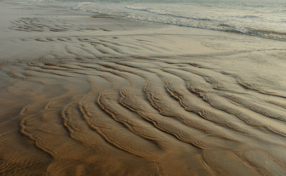 View of the wet sand with wavy patterns reflecting sunlight as the tide comes in creating a serene coastal scene Chiplun Maharashtra India. View of the wet sand with wavy patterns reflecting sunlight as the tide comes in creating a serene coastal scene Chiplun Maharashtra India.