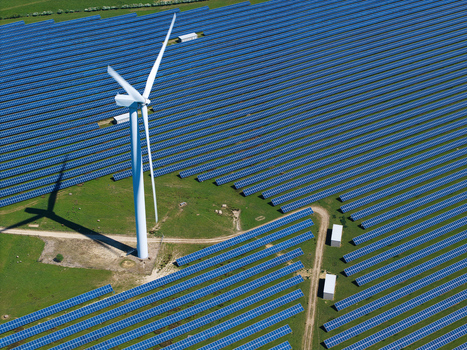 Aerial view of Chelveston Wind Farm featuring a tall wind turbine and vast rows of blue solar panels on green fields in Wellingborough England United Kingdom. Aerial view of Chelveston Wind Farm featuring a tall wind turbine and vast rows of blue solar panels on green fields in Wellingborough England United Kingdom.